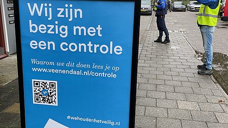 Op beeld is een stoepbord te zien met de tekst: "Wij zijn bezig met een controle. Waarom we dit doen lees je op www.veenendaal.nl/controle. Onderaan staat een QR-code die naar wehoudenhetveilig.nl gaat.