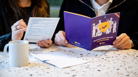 Op de foto zijn twee mensen te zien. De man rechts heeft een informatieboekje vast van Denk vooruit van de Rijksoverheid. Dit gaat over hoe je je voorbereid op een noodsituatie.